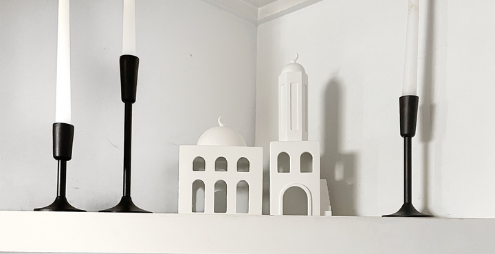 Mosque and minaret ceramic decorative statues on a bookshelf next to 3 candle holders