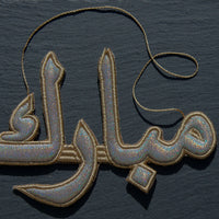 "مبارك" Mubarak Arabic Calligraphy Silver Embroidery Ornament On dark Background