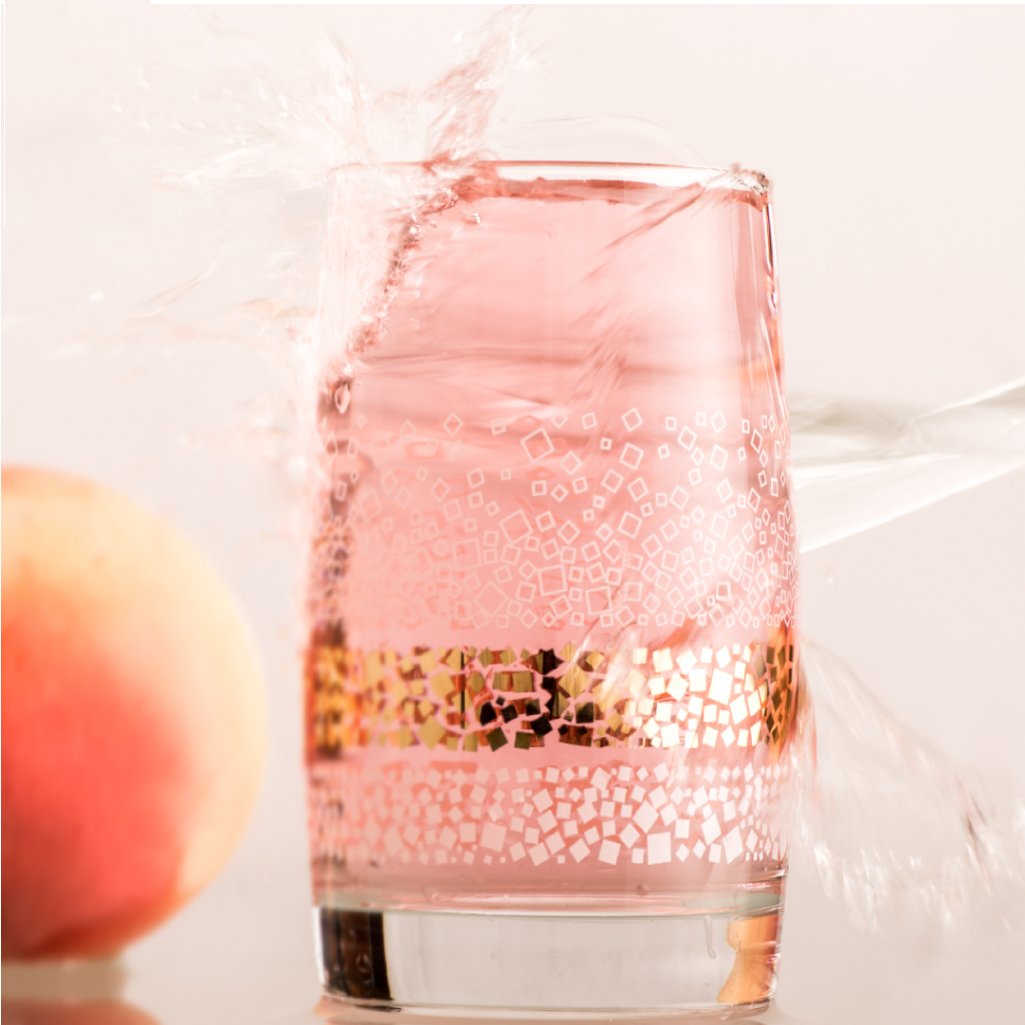 Transparent  glass dune tumbler with white and golden sands print filled with a pink color cold drink